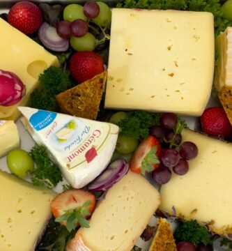 a variety of cheeses and fruits are arranged in a tray
