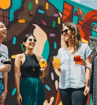 four women holding drinks while laughing together during daytime